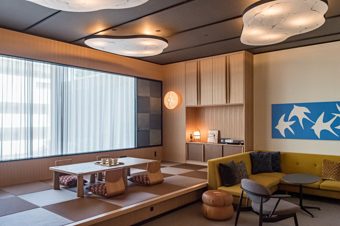 Modern hotel suite with tatami flooring, low wooden table, yellow sofa, and blue artwork with white bird silhouettes
