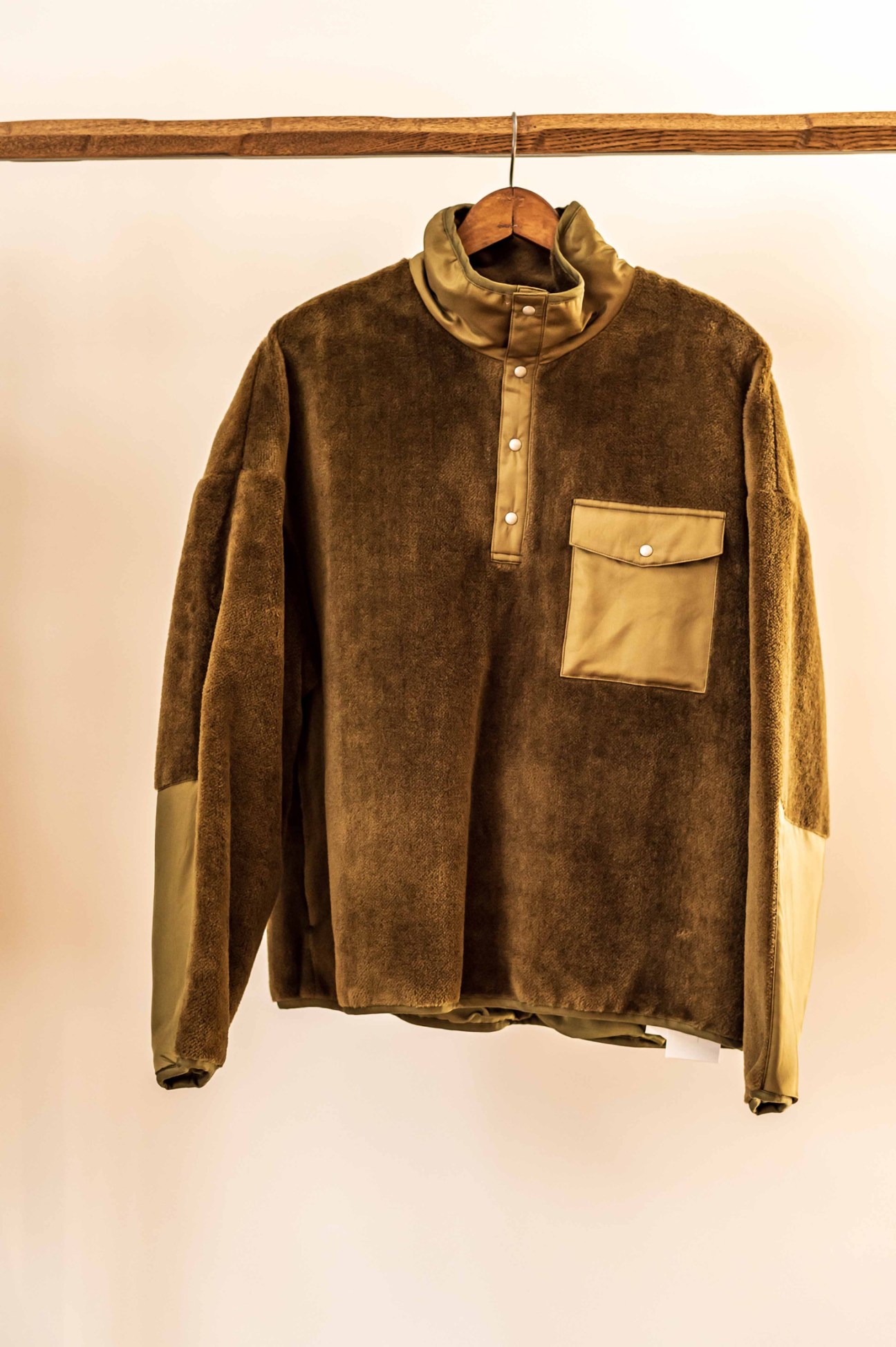 Brown fleece pullover with tan leather trim and snap button placket hanging on wooden hanger