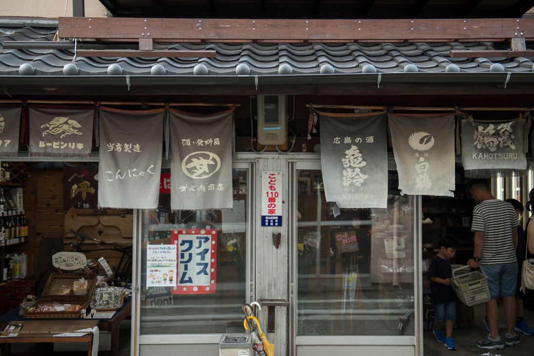 Traditional wooden storefront with draped fabric banners displaying Japanese text and sake brewery logos.