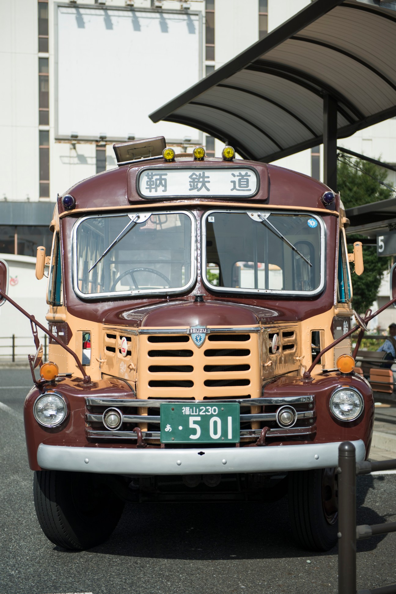 Vintage maroon and cream Isuzu bus with Japanese characters and yellow roof lights parked in Tomo, Japan.