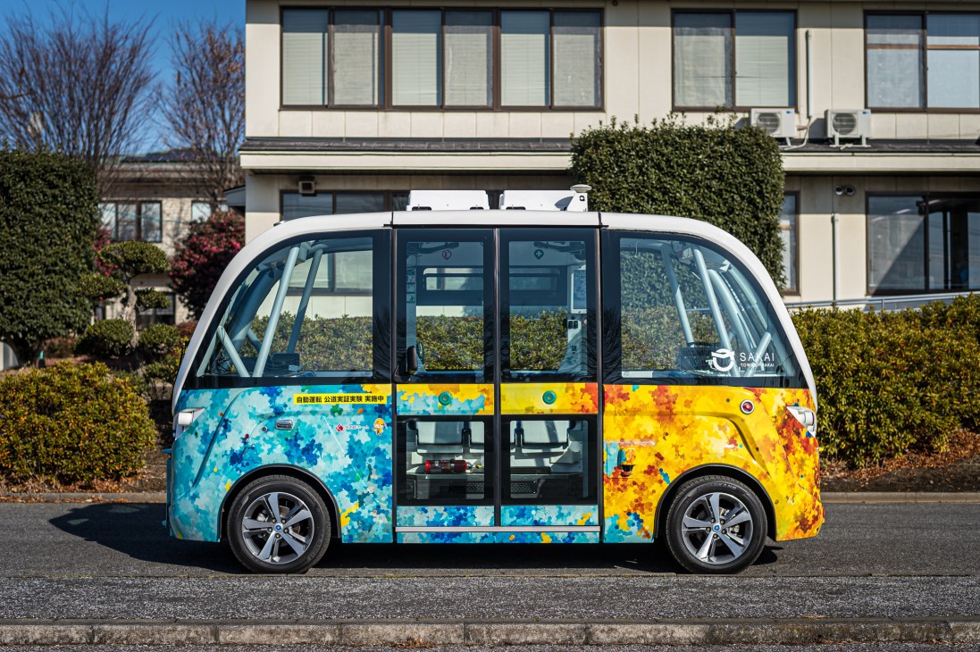 Brightly colored autonomous shuttle bus with blue and yellow paint design parked on street