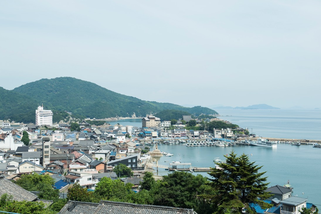 Coastal town of Tomo with traditional buildings nestled between forested hills overlooking the Seto Inland Sea.