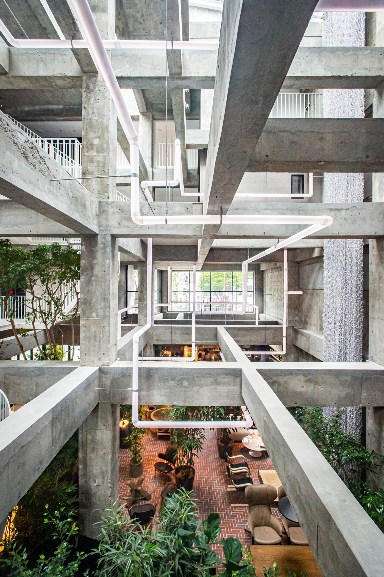 Multi-level concrete interior with exposed beams, white railings, brick flooring and furniture below