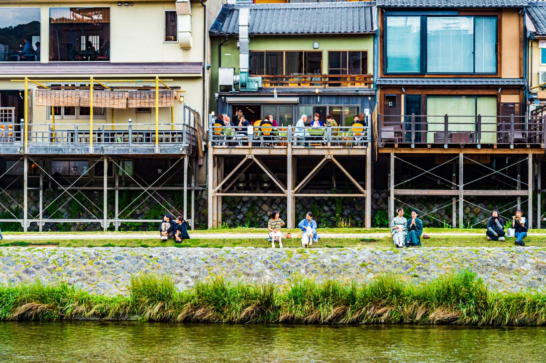 Riverside houses with traditional Asian architecture, people relaxing on grass and decks overlooking water