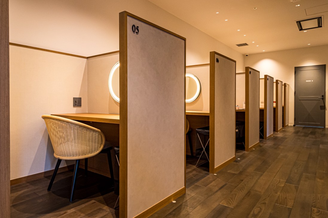 Row of numbered wooden cubicles with built-in desks, wicker chairs, and circular windows in modern co-working space