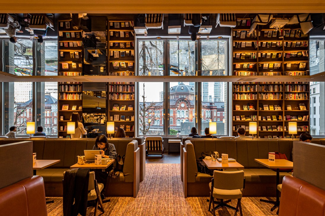 Interior view of Share Lounge Marunouchi showing café area with large windows overlooking Tokyo Station's red-brick façade