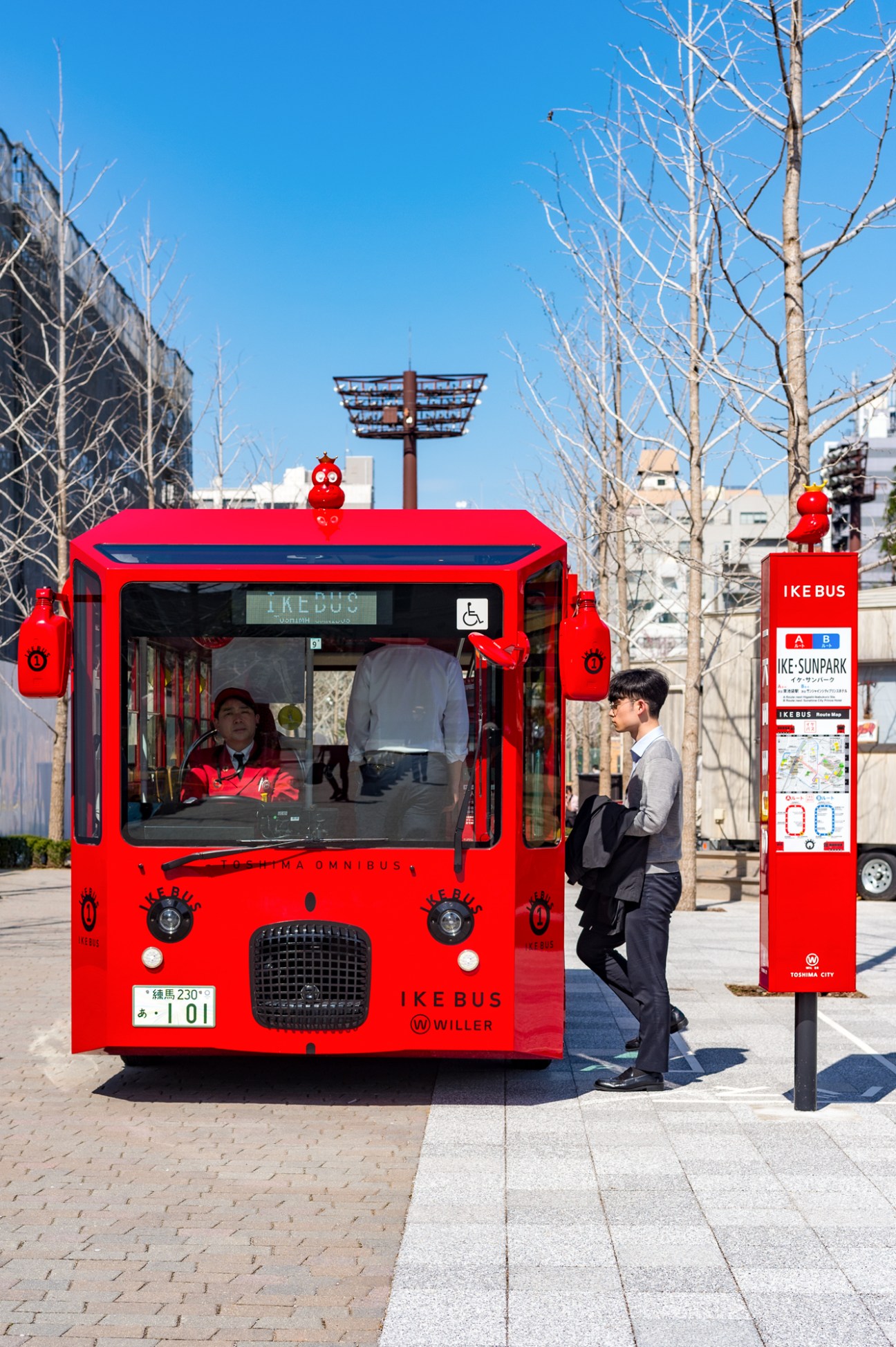 Red owl mascot Ike-chan sitting on top of bright red Ikebus electric bus