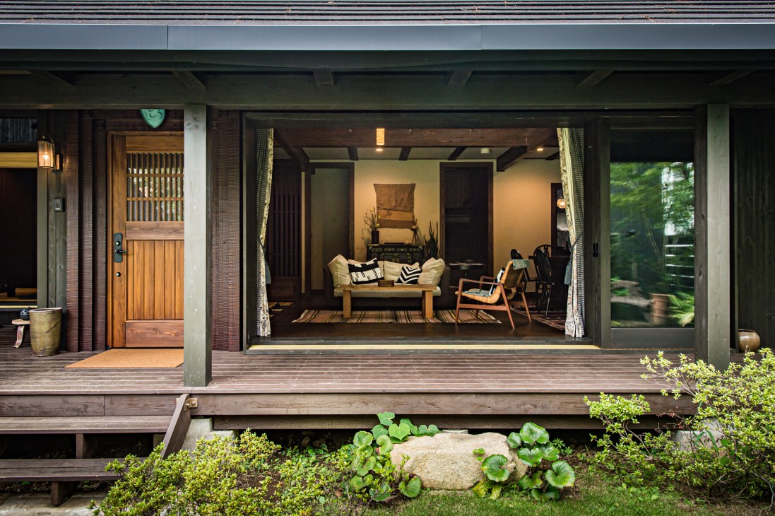 Modern log house with open terrace, sliding glass doors, wooden deck and furnished interior visible through windows.