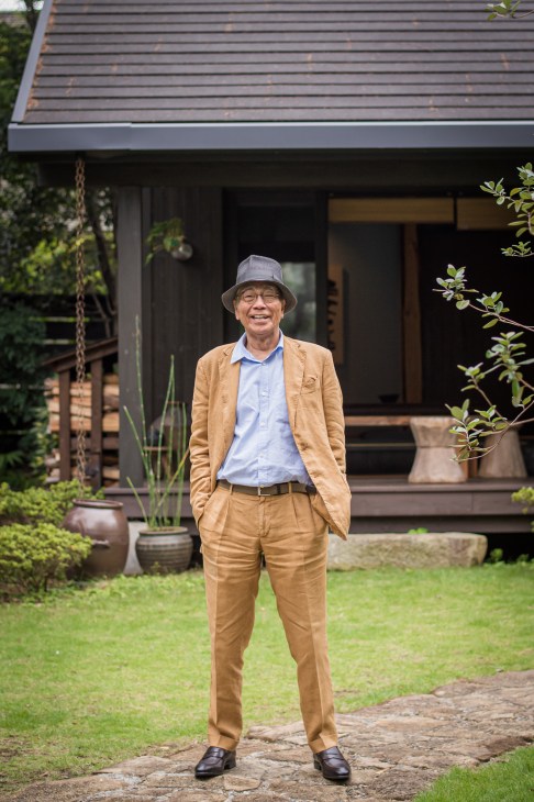 Kozo Futagi, 74-year-old CEO of Bess, standing in front of a modern log house wearing a tan suit and hat