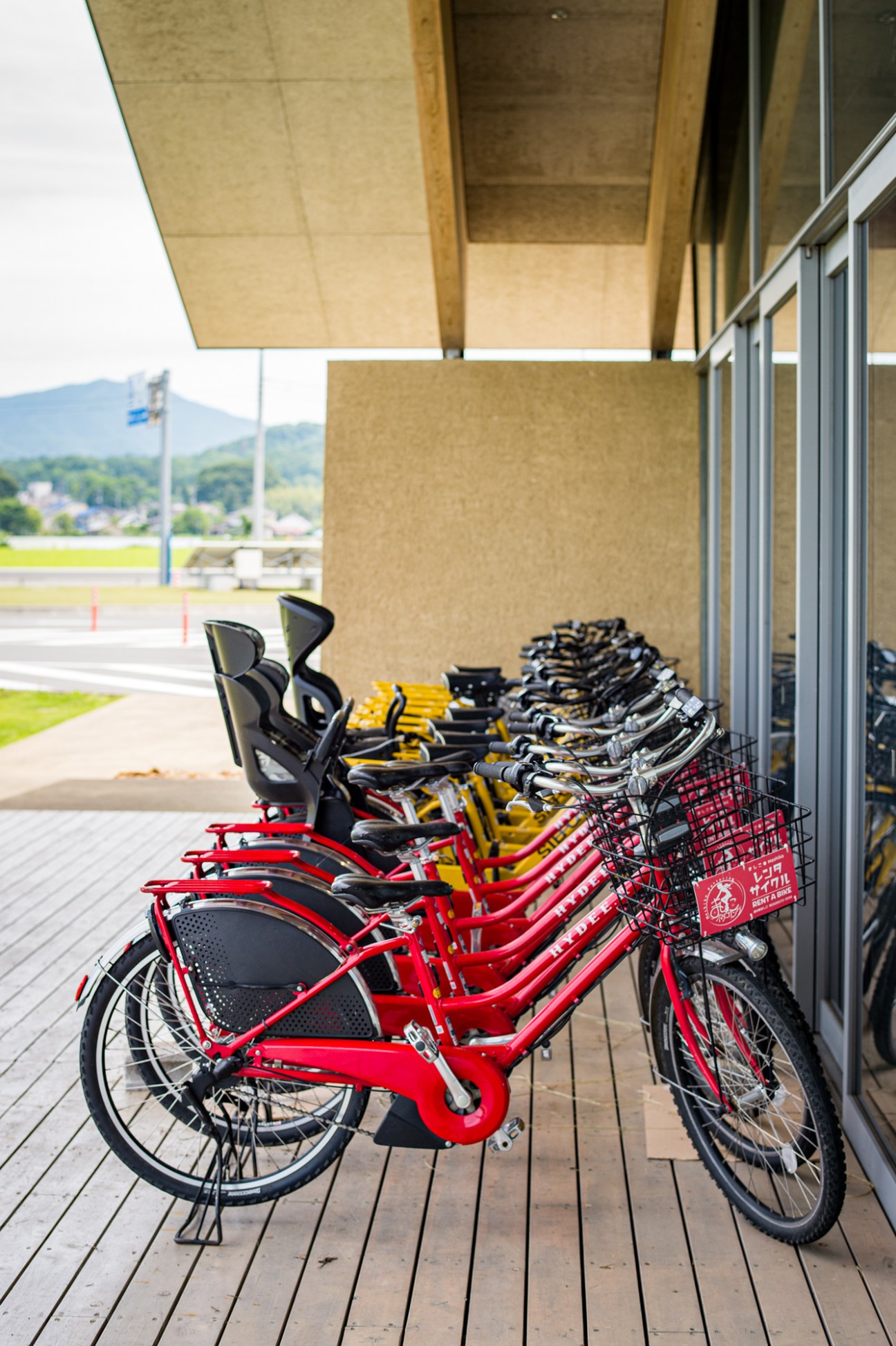 Red and yellow electric bikes lined up for hire under a covered structure at Mashiko Roadside Station.