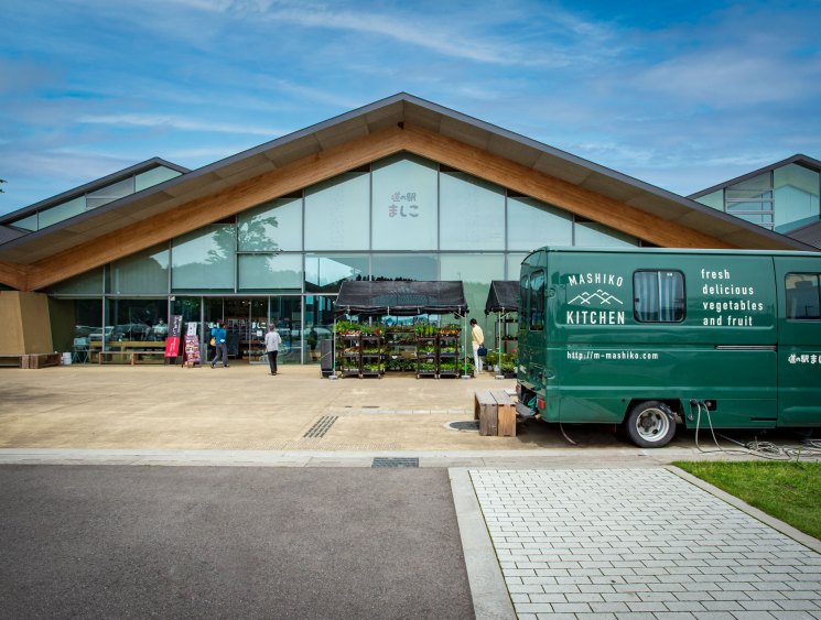 A green Mashiko Kitchen food van parked outside the modern wooden architecture of Mashiko Roadside Station in Japan.