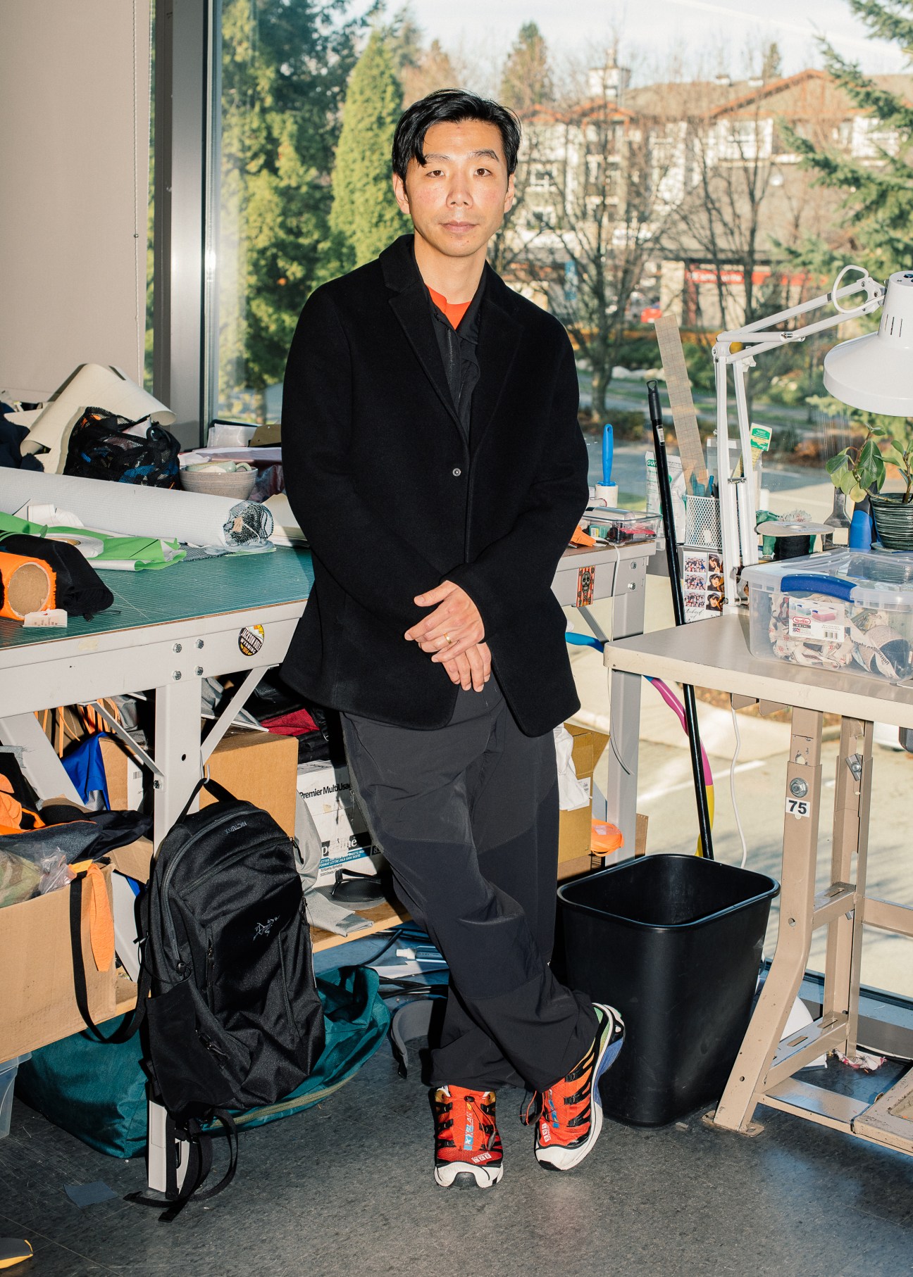 Man in black blazer standing in cluttered workshop space with equipment and storage
