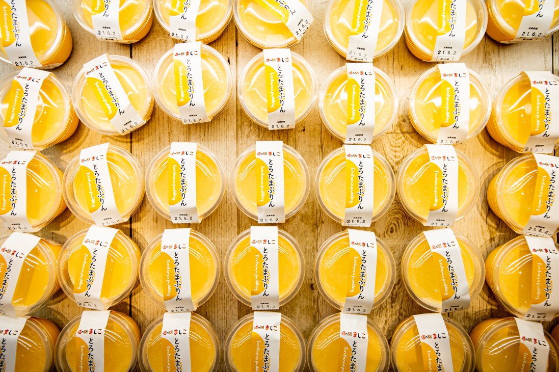 Multiple clear containers of yellow pudding with Japanese labels arranged on wooden surface.