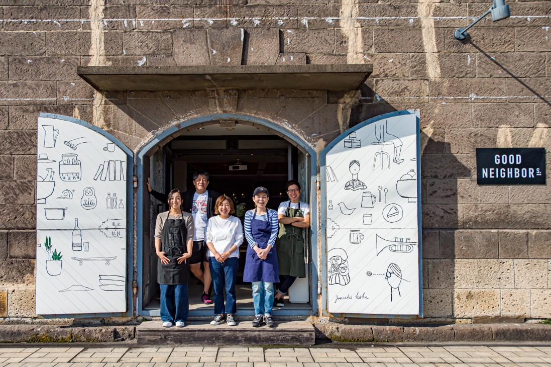 Five people standing in the doorway of Good Neighbors homeware shop with illustrated white doors