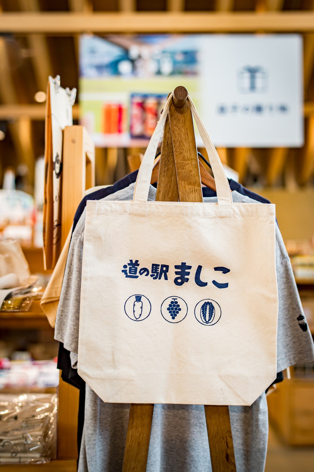 Cream-colored canvas tote bag with Japanese text and produce icons displayed on wooden stand.