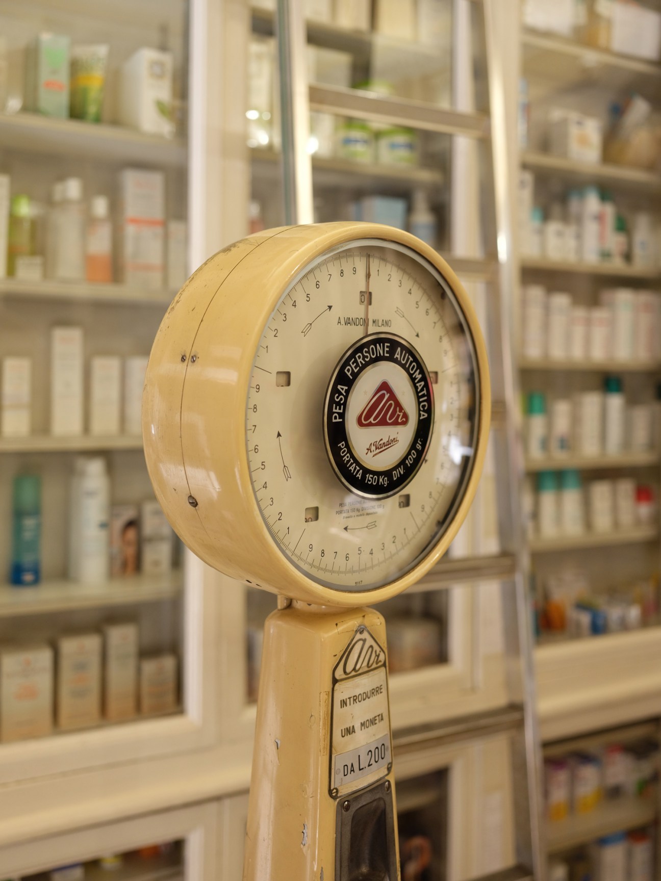 Vintage cream-coloured balance scale with Italian manufacturer branding in a pharmacy setting.
