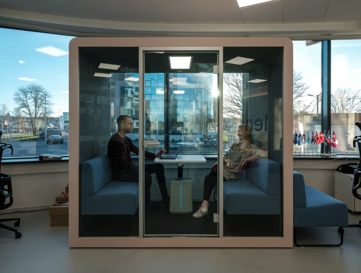 Two people talking in a glass meeting pod.