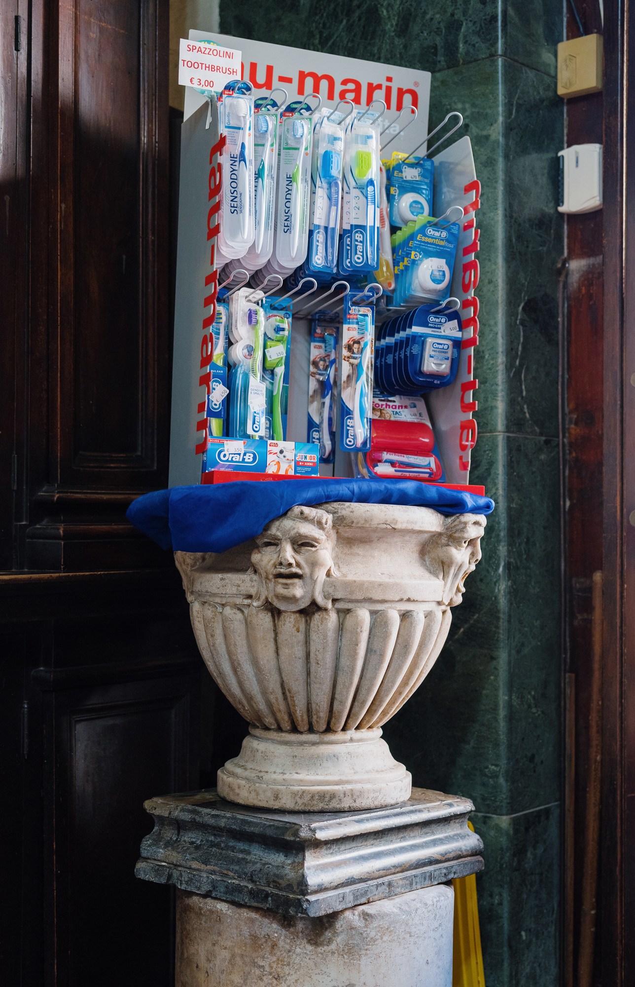 Display of Oral-B toothbrushes and dental products arranged on a decorative white stone urn with blue fabric.