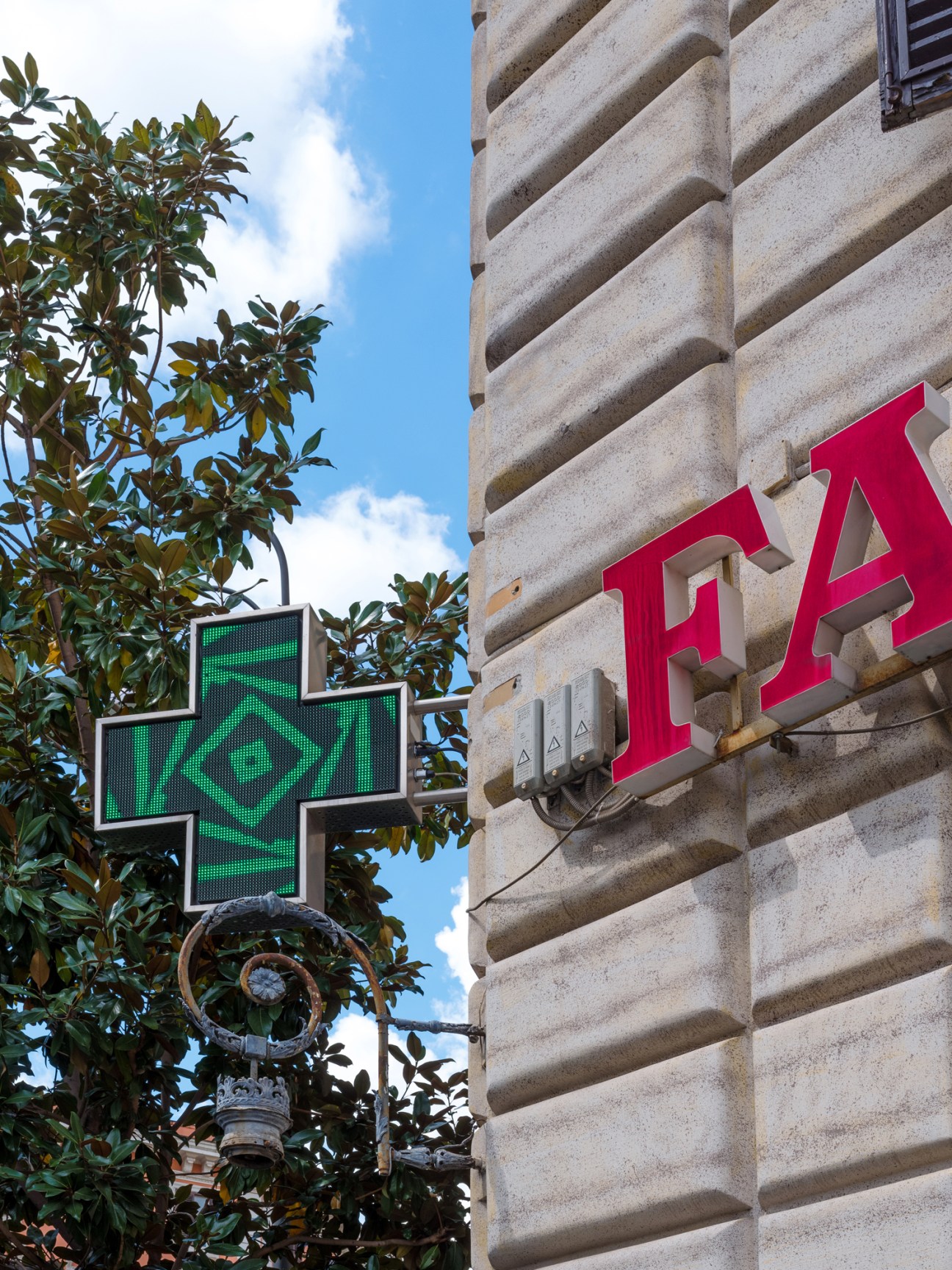 Green neon cross and pharmacy sign against stone building facade in Rome
