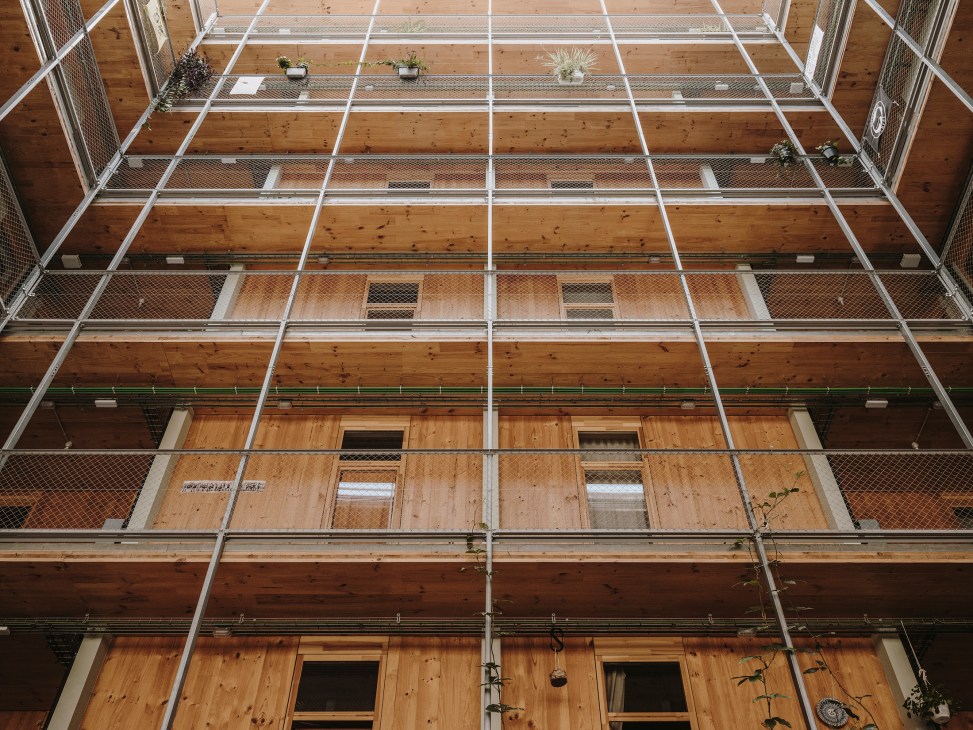 Upward view of La Borda's wooden façade and central courtyard with timber blinds and metal railings.