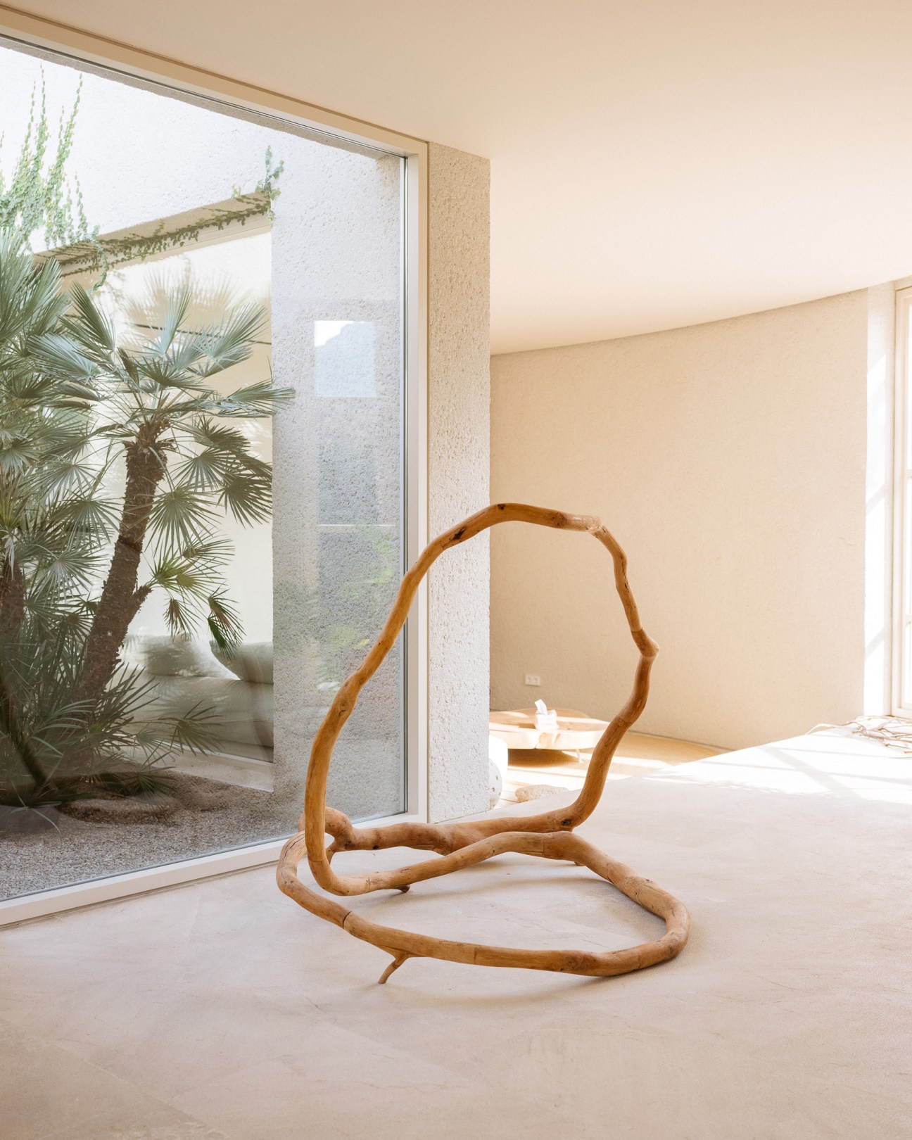 Curved sculptural artwork sits on floor of minimalist room with large windows overlooking palm trees and courtyard Artwork by Hiroshi Kitamura