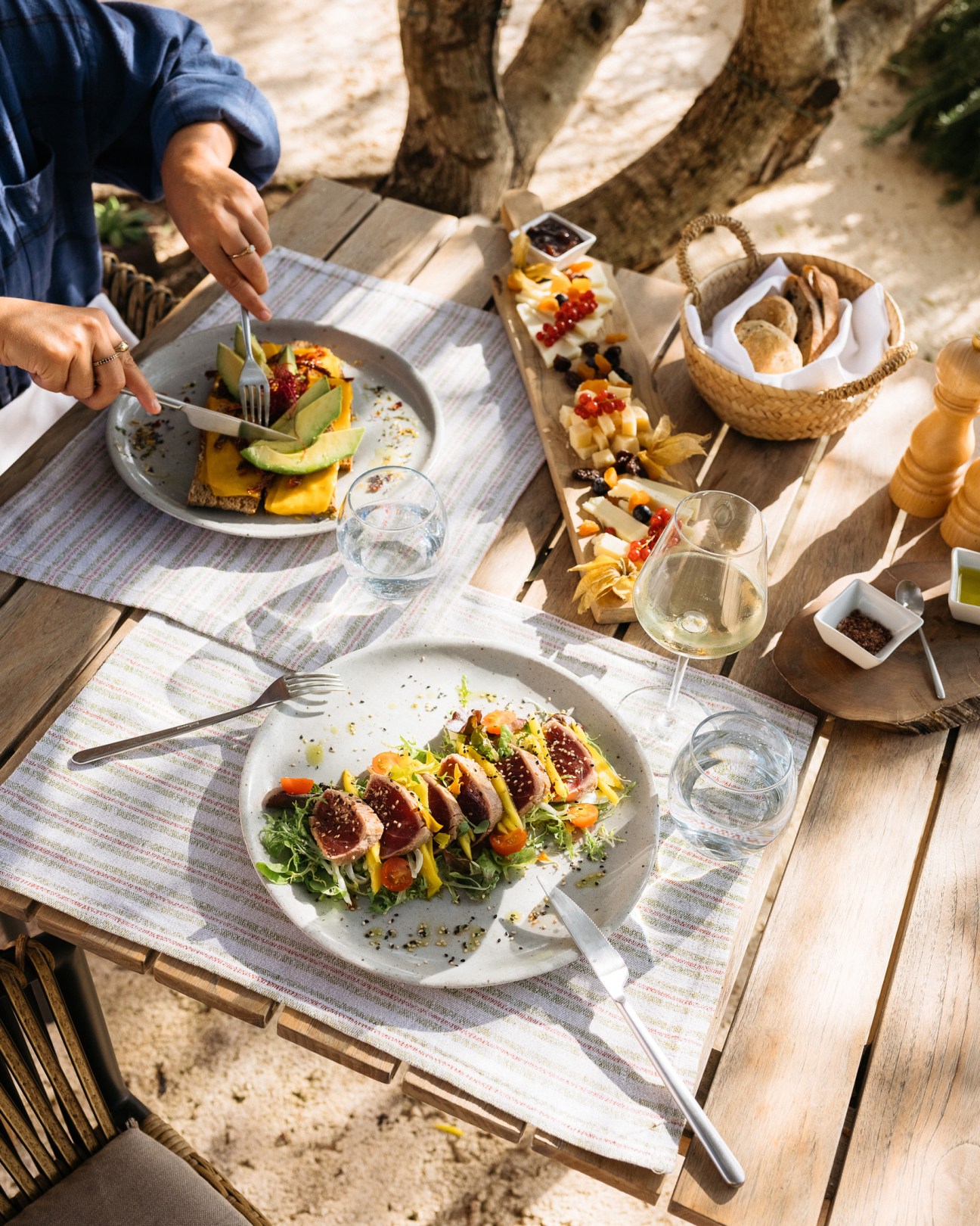 Overhead view of Mediterranean meal with fresh salad, avocado toast, charcuterie board and wine glasses on wooden table