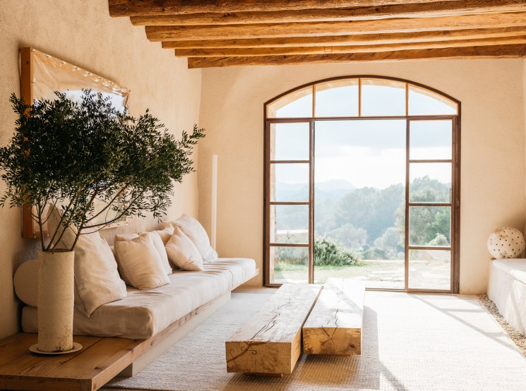 Minimalist living room with exposed wooden beams, cream sofa, large arched window overlooking countryside
