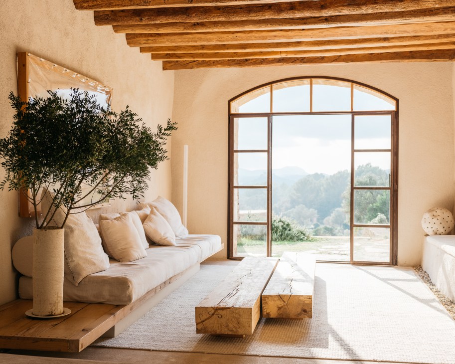 Minimalist living room with exposed wooden beams, cream sofa, large arched window overlooking countryside