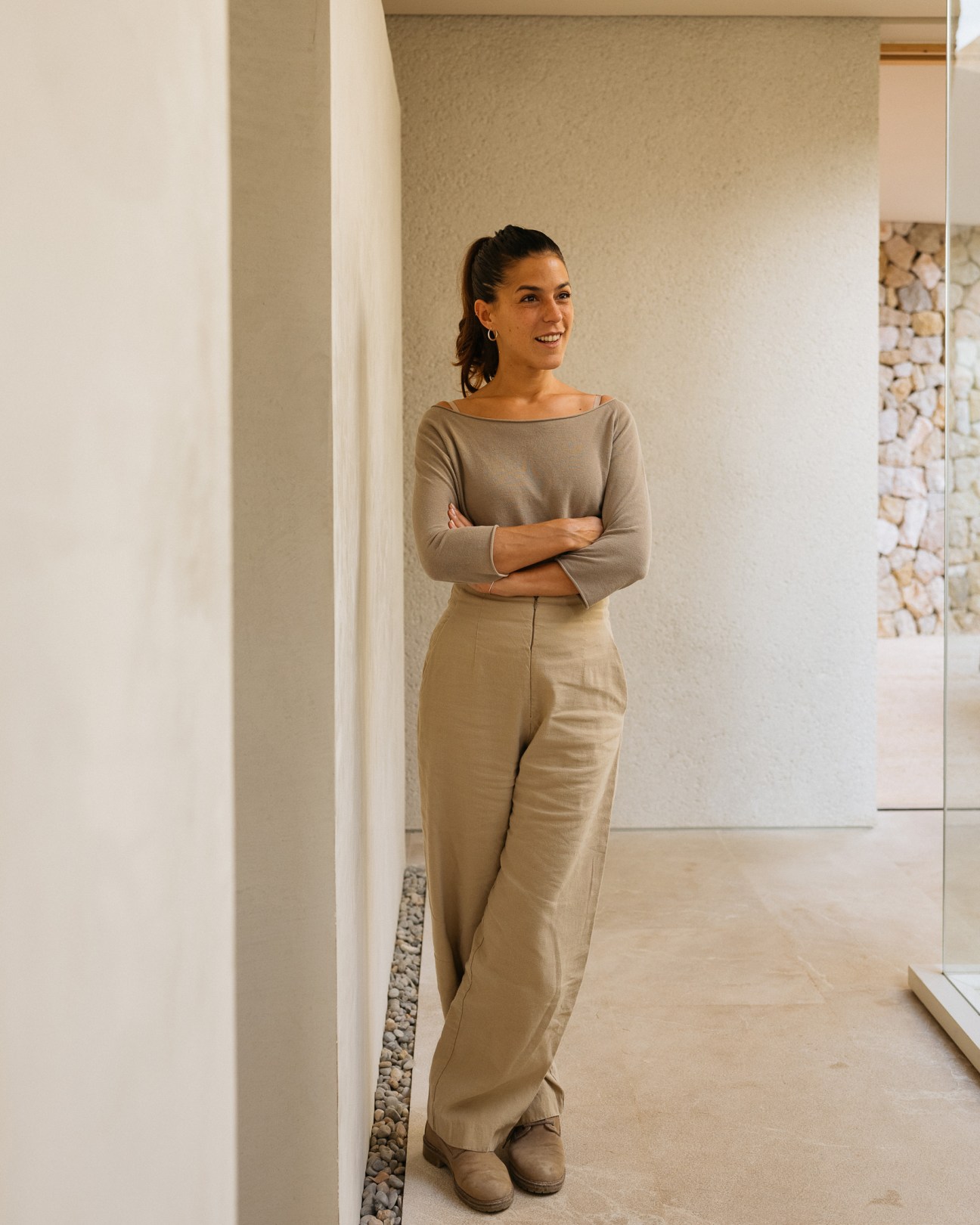 María Ríncon stands with crossed arms in a neutral-toned outfit in a modern interior with stone details