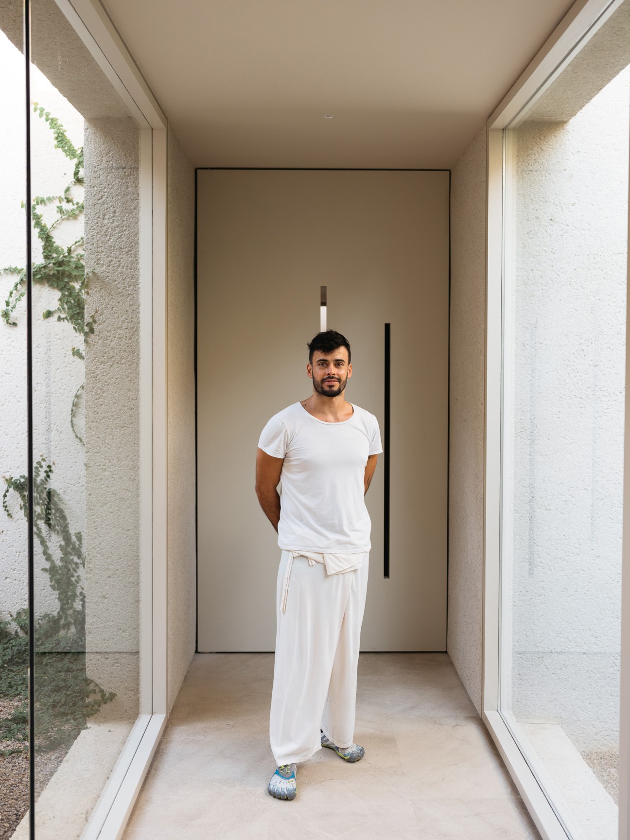 Man in white casual clothing stands in modern doorway of Es Racó d'Artà hotel in Mallorca