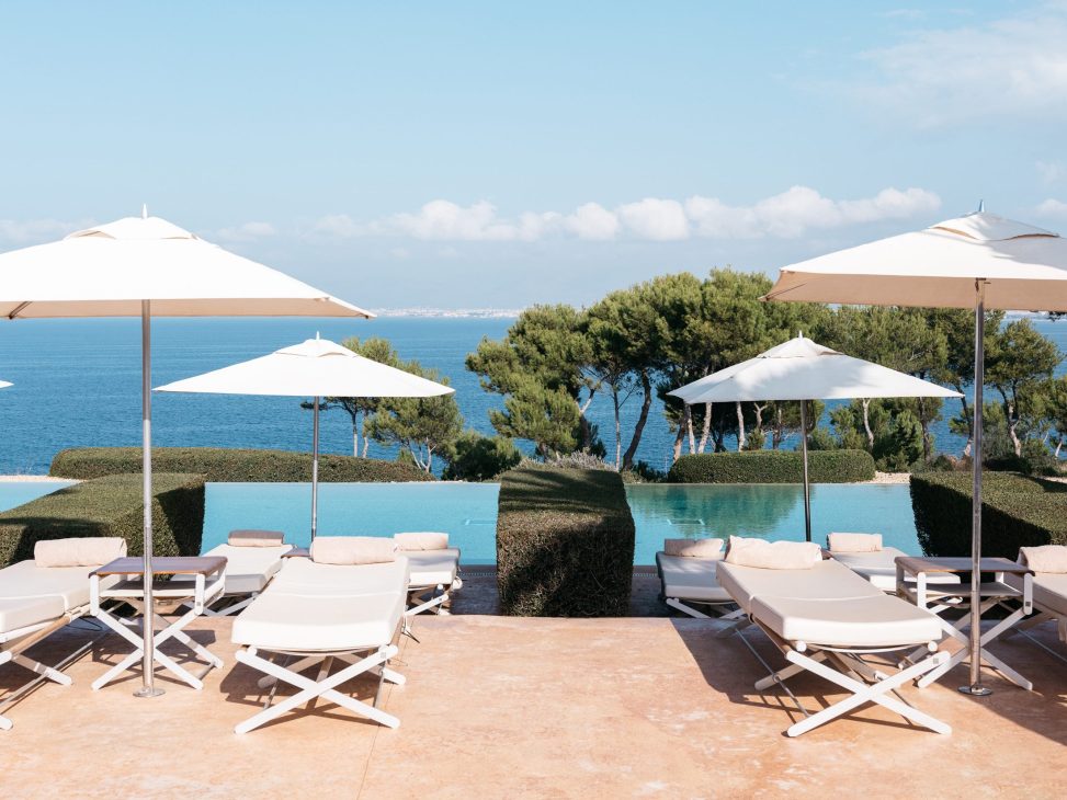 Luxury poolside loungers with white umbrellas overlooking Mediterranean sea and manicured hedges at Spanish resort