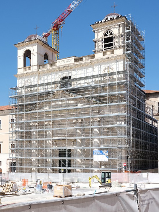Historic Italian cathedral covered in scaffolding during restoration work with construction crane and equipment visible