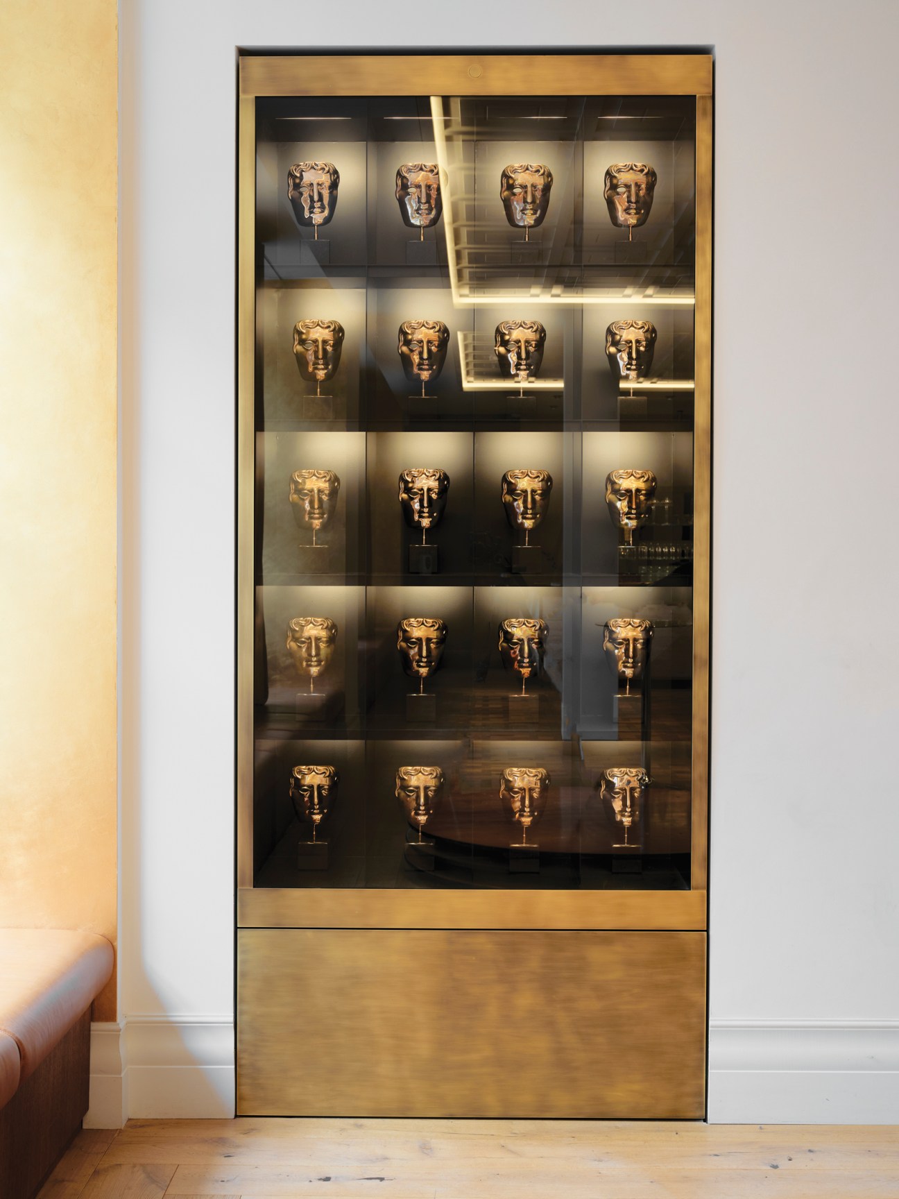 Glass display cabinet with five rows of golden BAFTA award masks arranged on illuminated shelves