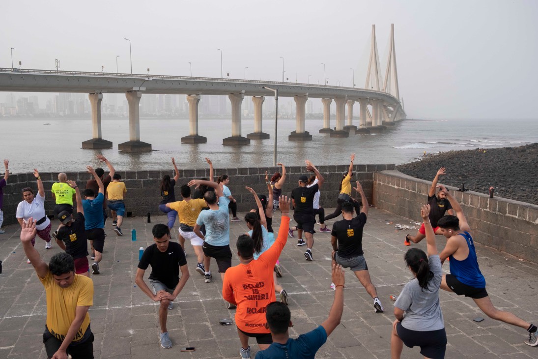 Group of runners doing stretching exercises on a waterfront promenade with a large bridge in the background
