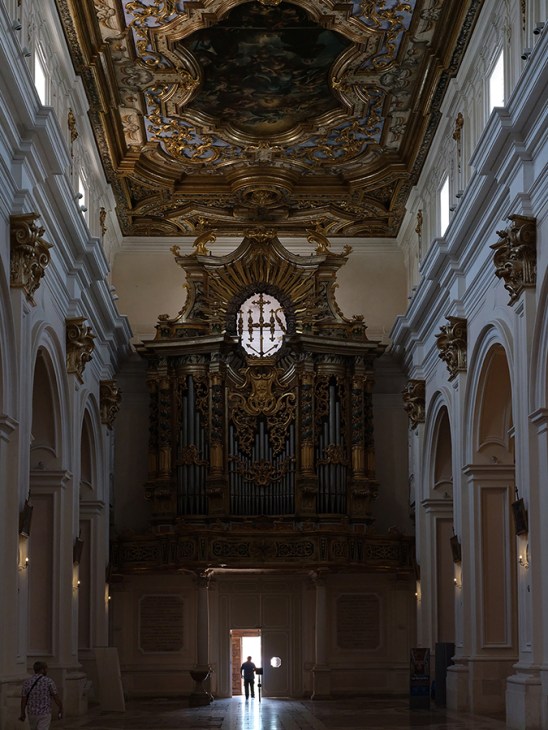 Basilica of San Bernardino interior ornate baroque church showing elaborate pipe organ, decorated ceiling, white columns and lone visitor