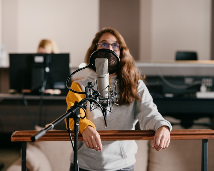 Voice actor wearing headphones speaks into a microphone in a professional dubbing studio.