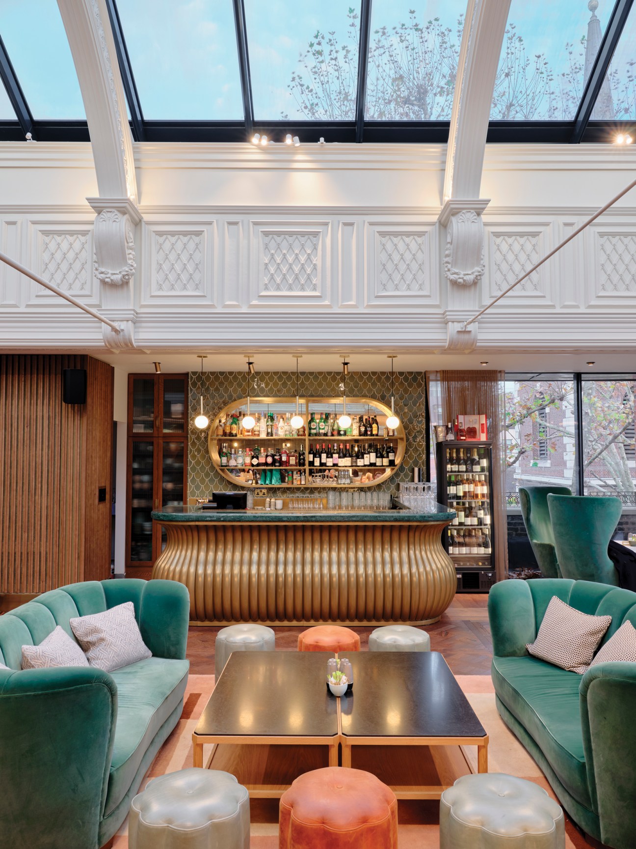 Luxurious members' lounge with green velvet seating, glass ceiling, ornate bar, and art deco-inspired design