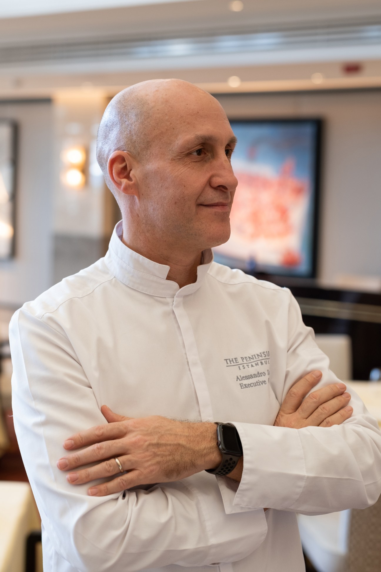 Chef Alessandro Santi in white Peninsula hotel uniform with arms crossed looking to the side in professional kitchen setting