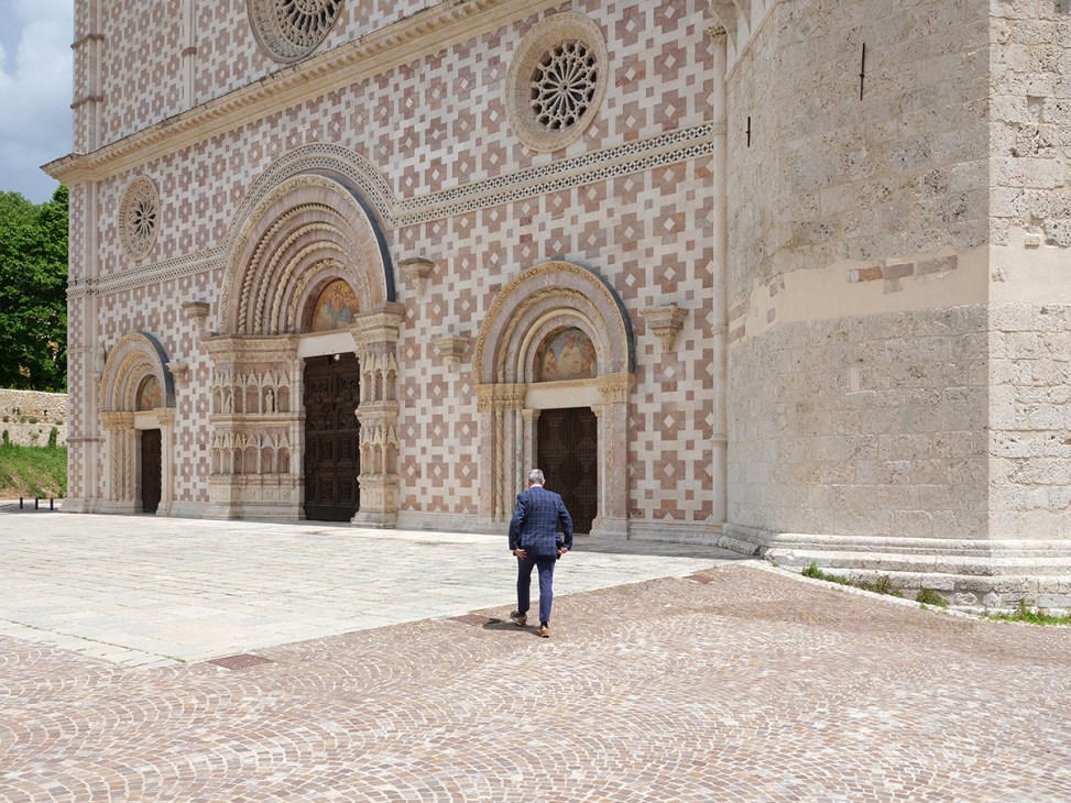 Person walking across cobblestone plaza toward ornate facade of restored basilica with pink and white geometric patterns