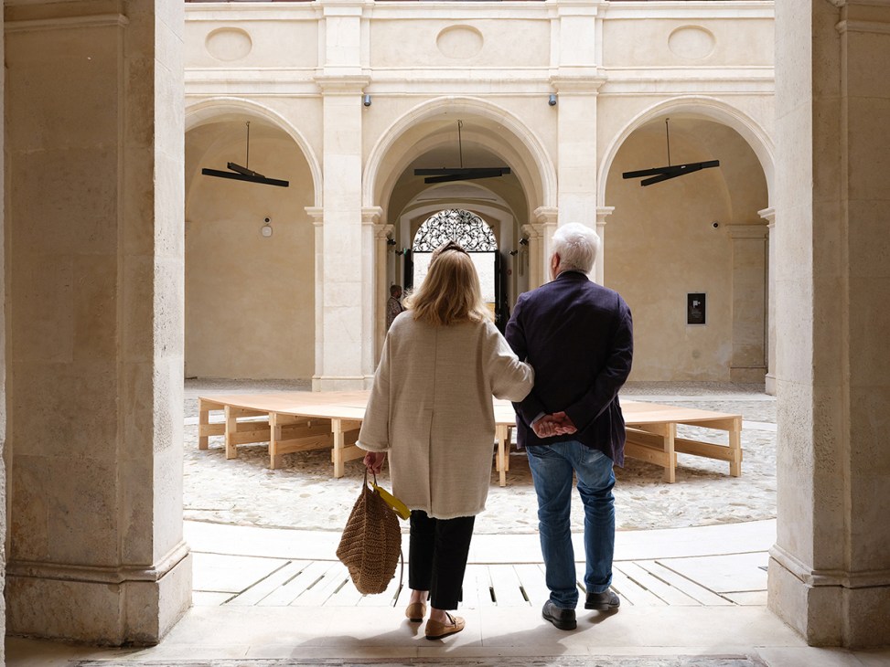 Two visitors walk through arched colonnade of Maxxi museum with classical architecture and wooden benches
