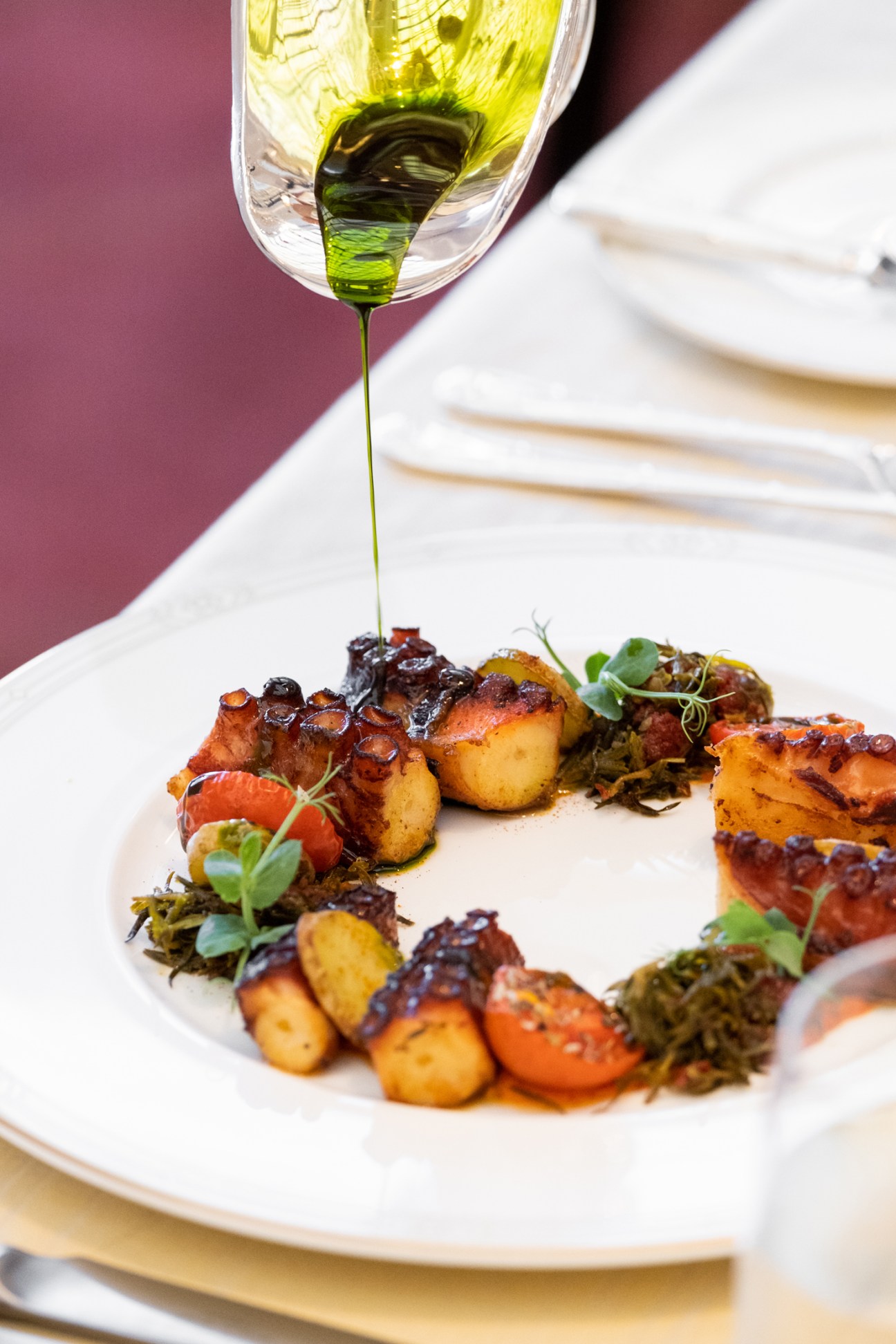 Green olive oil being drizzled over seared scallops with vegetables and microgreens on white plate