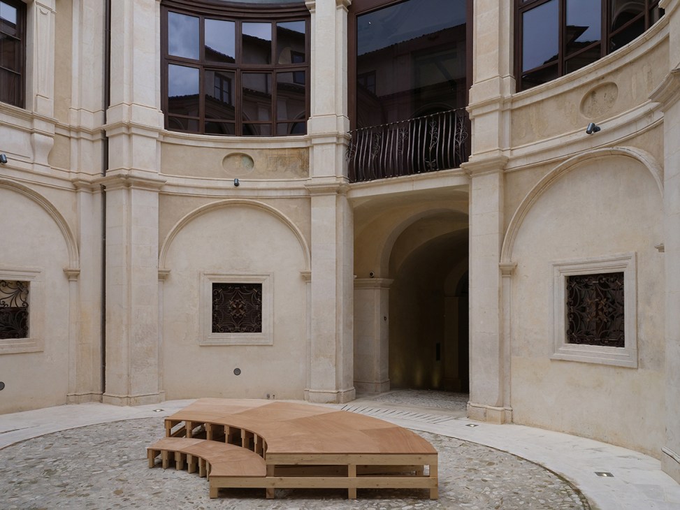 Stone courtyard with arched colonnade and wooden sculptural installation in renovated Italian museum