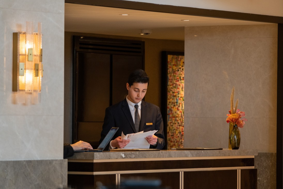 Hotel reception desk with marble surfaces and staff member in dark suit reading documents in elegant lobby