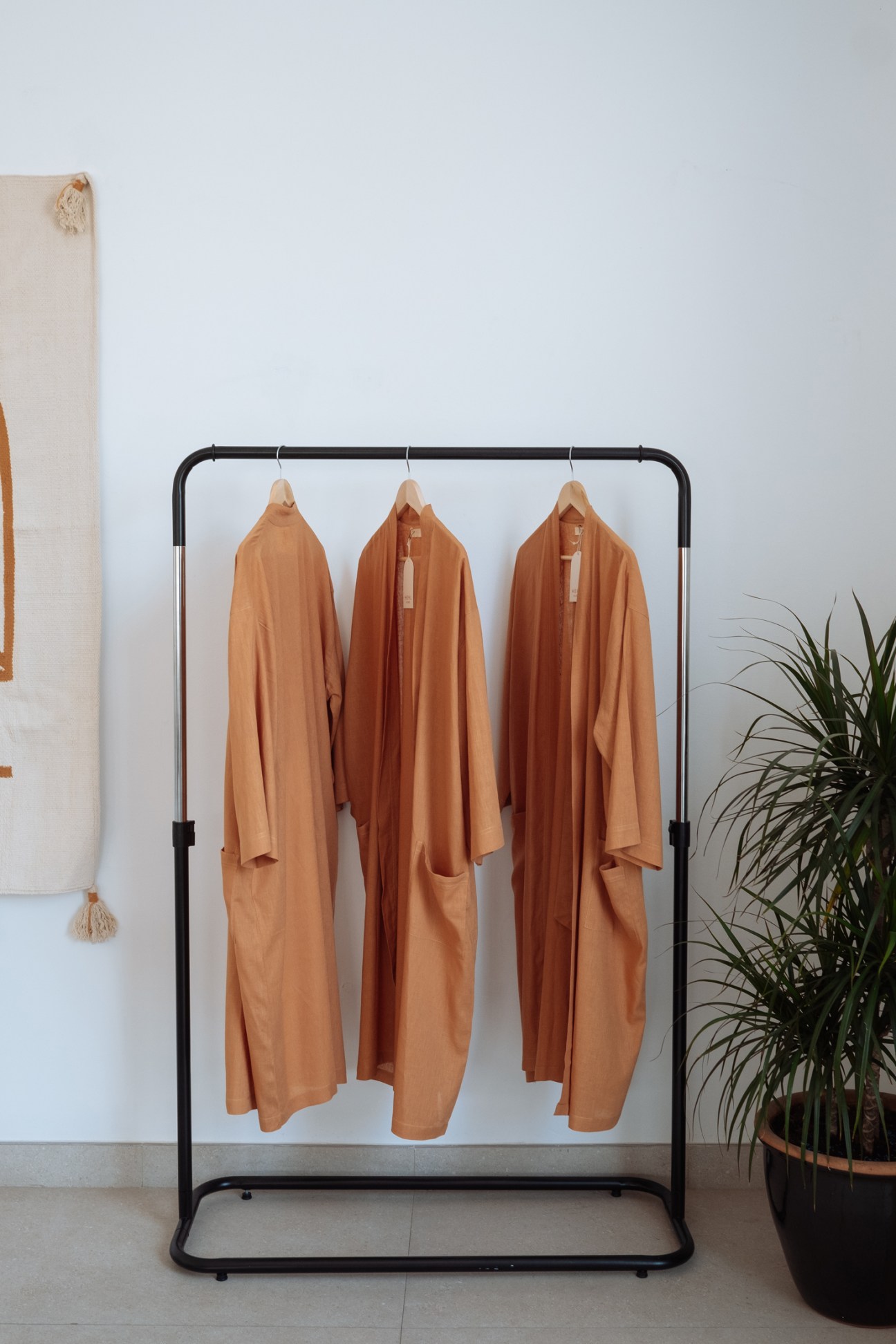 Three earth-tone garments hanging on a black metal rack in a minimalist retail space