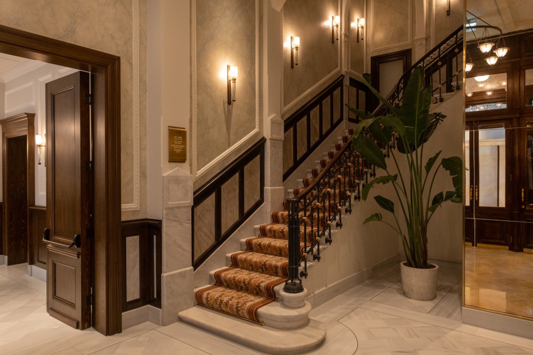 Elegant hotel lobby staircase with ornate iron railings, patterned carpet runner, and warm lighting in luxurious interior