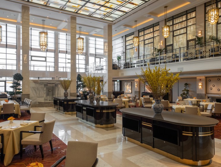 Grand hotel lobby with geometric stained-glass ceiling, marble floors, pendant lights, and dining areas