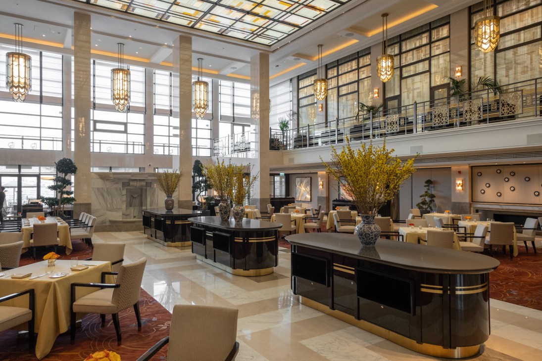 Grand hotel lobby with geometric stained-glass ceiling, marble floors, pendant lights, and dining areas