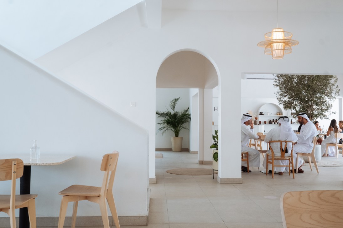 Bright, minimalist café interior with wooden chairs, arched doorways, and diners enjoying breakfast at Heal restaurant.