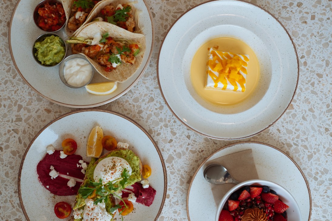 Overhead view of four plated dishes on a terrazzo table including tacos, soup, and a beet salad.