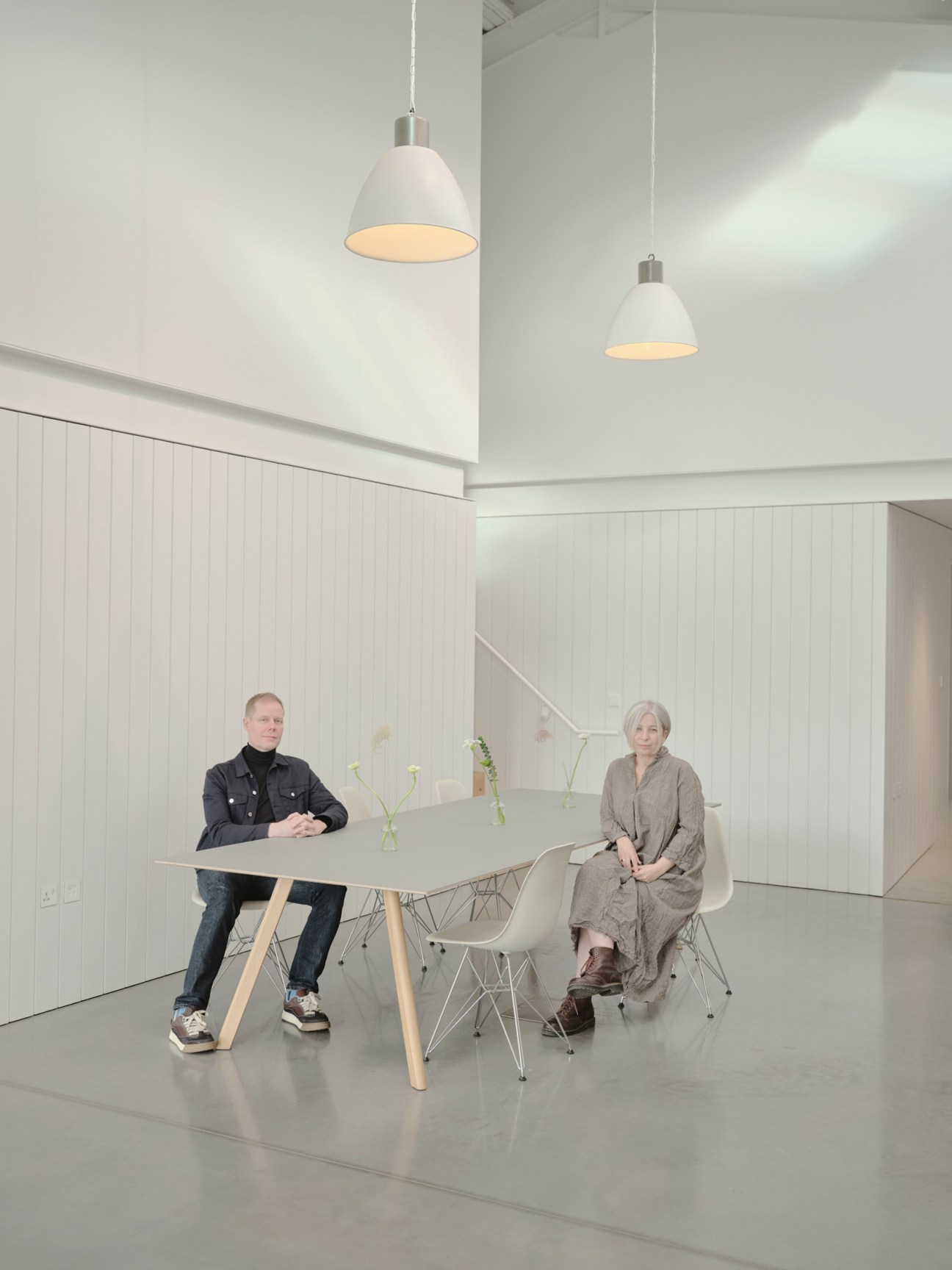 Composer Max Richter and artist Yulia Mahr sit at a table in a minimalist white interior space with pendant lights.